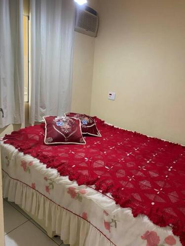 a bed with a red comforter and pillows on it at Apartamento Encantador B in Montes Claros