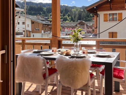 une table avec des chaises blanches assises sur un balcon dans l'établissement Appartement cosy, 2 suites, terrasse, centre Les Gets - FR-1-598-154, aux Gets