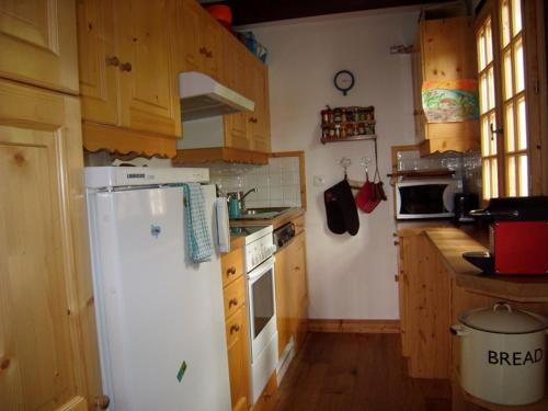 La cuisine est équipée d'un réfrigérateur blanc et de placards en bois. dans l'établissement Chalet 5 chambres, 9 pers, wifi, 1 animal, non fumeur - FR-1-733-144, à Crest-Voland
