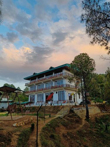 a large white building with a tree in front of it at Lap Of Himalayas Resort in Kausani
