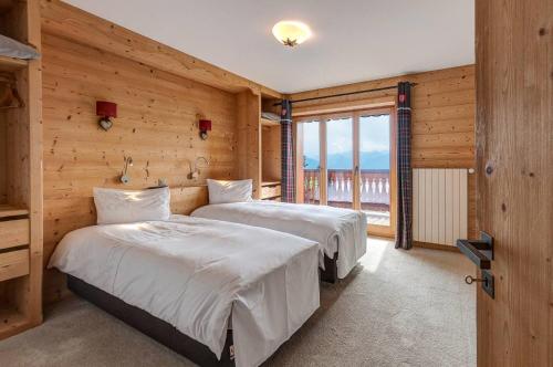 two beds in a room with wooden walls and a window at Alpe Fleurie Residence in Villars-sur-Ollon