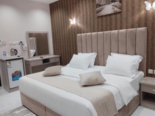um quarto com uma cama grande com lençóis brancos e almofadas em العلي للشقق المخدومة Alalihotel em Hafr Al-Batin
