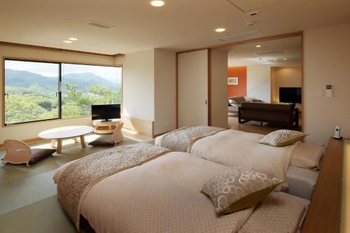 a bedroom with two beds and a living room with a view at 仙台秋保温泉 篝火の湯 緑水亭 in Sendai