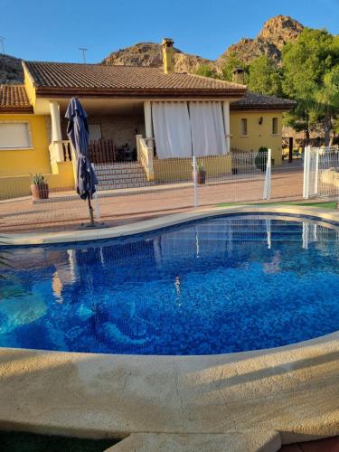 a swimming pool with an umbrella in front of a house at Casa Rural Familiar Piscina Sierra Balumba in Cobatillas