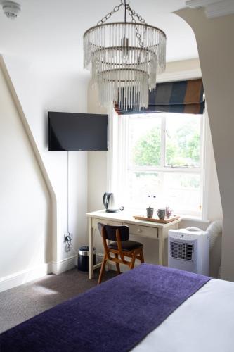 a bedroom with a bed and a desk and a chandelier at Kew Gardens Hotel in Kew