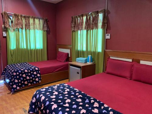2 Betten in einem Zimmer mit roten Wänden und grünen Vorhängen in der Unterkunft Pondok Sri Salang in Kampong Telok Salang