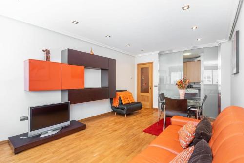 sala de estar con sofá naranja y TV en Apartamento con garaje, en Luanco