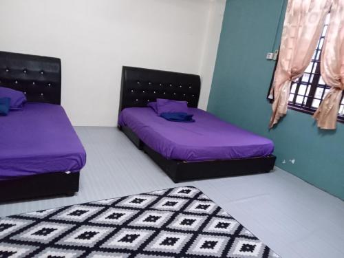2 Betten in einem Zimmer mit lila Bettwäsche und einem Teppich in der Unterkunft Cuti2 Homestay KT in Kuala Terengganu