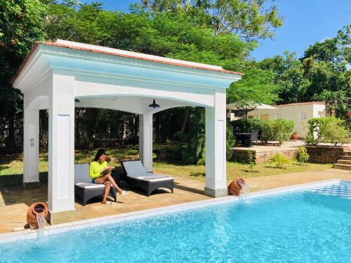 a woman sitting under a pavilion next to a swimming pool at Hilda's Homestay in Diani Beach