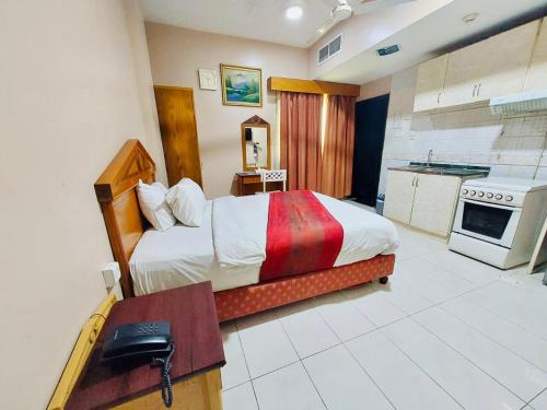 Al Ghadeer Hotel Apartment في الشارقة: غرفة نوم بسرير ومكتب ومطبخ