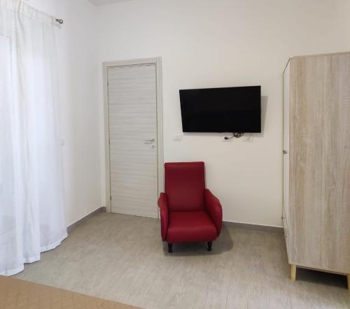 Cette chambre comprend une chaise rouge et une télévision murale. dans l'établissement Il Cardinale, à Reggio de Calabre