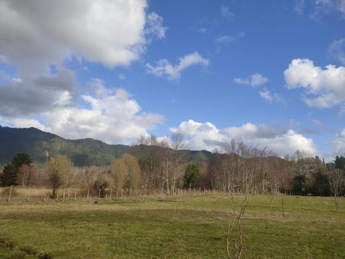 a field with trees and mountains in the background at Cabaña Precordillera Cunco in Cunco