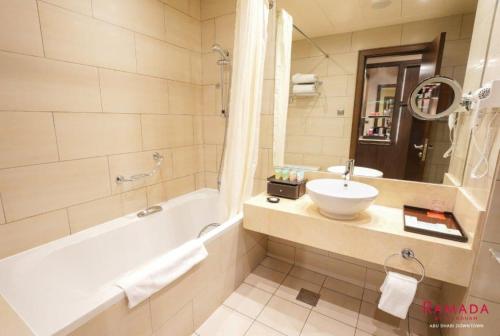 y baño con bañera, lavabo y espejo. en Ramada Downtown Abu Dhabi en Abu Dabi