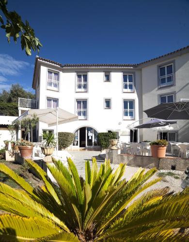 a large white building with plants in front of it at Hotel St Joseph in Algajola