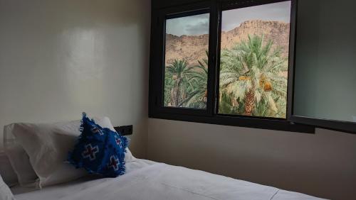 a bedroom with a bed and two windows with palm trees at Hotel AZUL Todra Gorges in Tinerhir