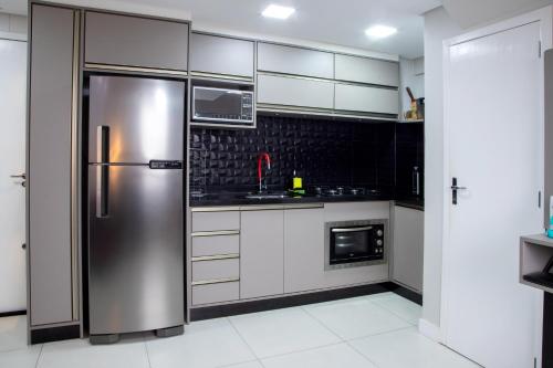 - un réfrigérateur en acier inoxydable dans une cuisine avec des placards blancs dans l'établissement Pequeno Paraíso Loft - Praia da Cal, à Torres