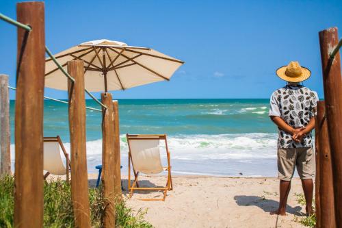 Vivá Barra Hotel Pousada في بارا دي ساو ميجيل: رجل يقف على شاطئ فيه مظلة وكراسي