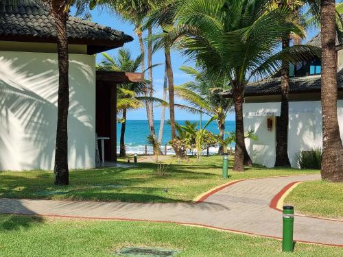 a walkway leading to a resort with palm trees and the ocean at Flat ou Bangalo Luxo Beach Class Beira Mar Muro Alto in Porto De Galinhas