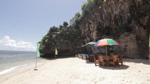 a beach with tables and chairs and an umbrella at Gratum Beach Resort in Dapitan