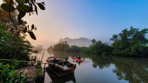 a boat sitting on a river with trees and a mistyermottermott at Singharaja Garden AGRO ECO Lodge in Pelawatta