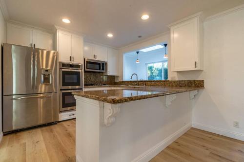 a kitchen with white cabinets and a stainless steel refrigerator at Modern 3 King Beds, Beautiful Large Backyard, WFH, Long Stays, Waterfall, WI-FI, FWY, 25 mins to Beach in Thousand Oaks