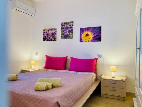 um quarto com uma cama com almofadas cor-de-rosa e pinturas na parede em SU GIUALI em SantʼAnna Arresi