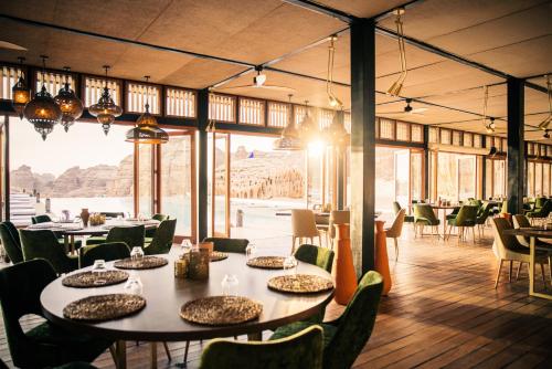 Our Habitas AlUla في العلا: غرفة طعام بها طاولات وكراسي ونوافذ كبيرة