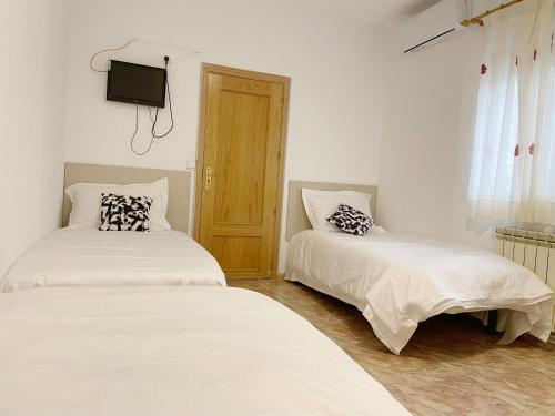 two beds in a room with a tv on the wall at Pensión el Carmen in Alcobendas
