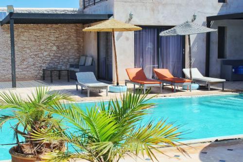 a swimming pool with chairs and umbrellas next to at Villa Sarah in Sidi Kouaki