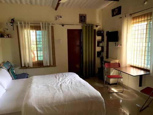 a bedroom with a bed and a desk and windows at Sattva Farmstay in Bangalore