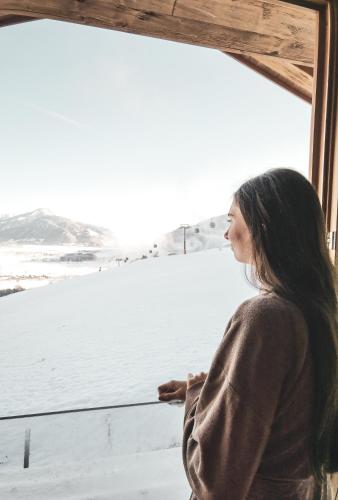 a woman looking out of a window at the snow at ZAGLGUT HOTEL-CHALETS Wellness & Views with Summer Card Included in Kaprun