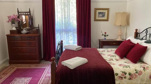 a bedroom with a bed with red curtains and a dresser at Freida - Historic Farmhouse Bellingen in Gleniffer