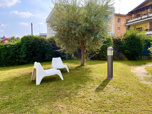 two white chairs sitting in the grass near a tree at Case vacanza le vele in Desenzano del Garda