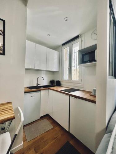 une cuisine avec des armoires blanches, un évier et une fenêtre dans l'établissement Très beau studio refait à neuf 2, à Saint-Ouen
