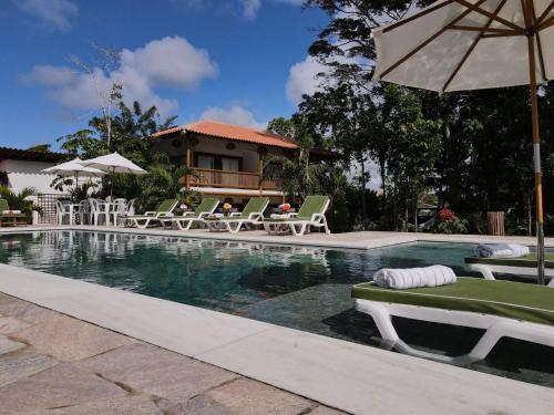 a swimming pool with lawn chairs and an umbrella at Pousada Recanto Caxando in Trancoso