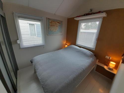 a small bedroom with a bed and two windows at Beautiful 6-person chalet with Finnish wood-fired sauna in Tzummarum