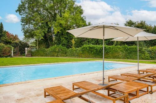 a pool with chairs and an umbrella next to a swimming pool at Villa Paséo - 11 Bedrooms - Large Heated Swimming Pool - Near Deauville in Bonneville-sur-Touques