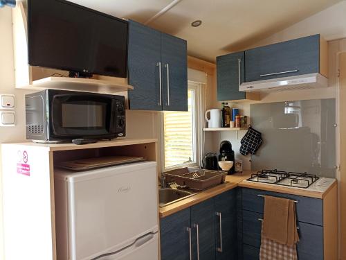 a kitchen with blue cabinets and a microwave and a refrigerator at Camping Domaine des Iscles in La Roque-dʼAnthéron
