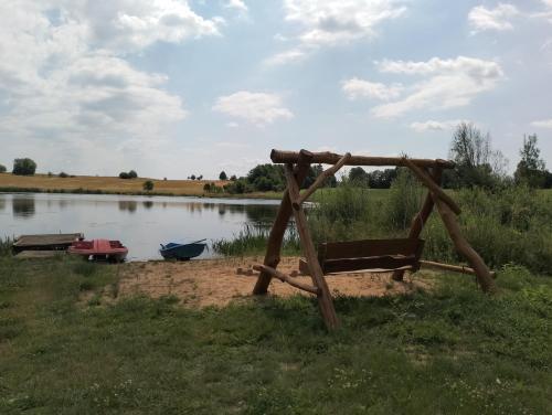 a wooden bench next to a lake with a boat at Domek Nad Stawem in Gołdap
