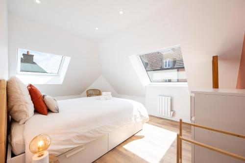 a white bedroom with a bed and two windows at Duplex Petit-Fort proche plage in Gravelines