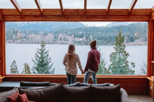 two people looking out of a large window at a lake at Peninsula Petit in San Carlos de Bariloche