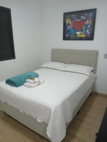 ein Bett mit weißer Bettwäsche und ein Gemälde an der Wand in der Unterkunft Apartamento condomínio Taboão da Serra/ familysnow in Taboão da Serra