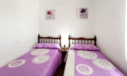 2 bedden in een kleine kamer met paarse lakens bij CASA RASPA, BATERNA (ÁVILA) in Baterna