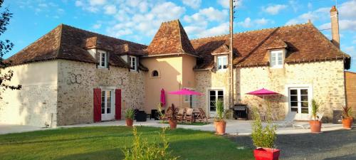 una gran casa de piedra con sombrillas rosas en el patio en Gîte & chambre d'hôtes du Moulin, en Brûlon