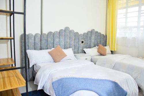 Executive Two & Three Bedroom Suites في ناكورو: غرفة نوم بسريرين مع شراشف بيضاء ومخدات برتقالية