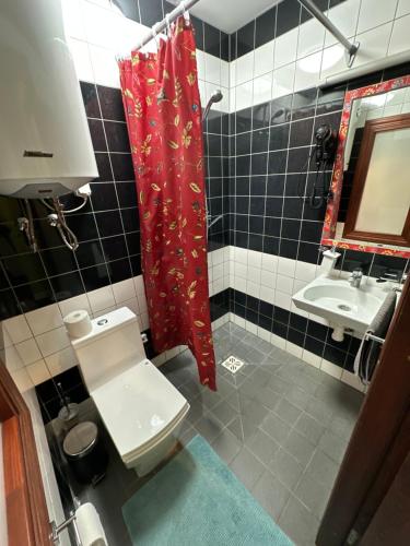 uma casa de banho com um WC e uma cortina de chuveiro vermelha. em Viesnīcas Jolanta apartamenti em Kolberģi