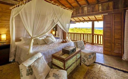 a bedroom with a canopy bed with chairs and a table at Casa Eliza Trancoso, casa de luxo com vista mar in Trancoso