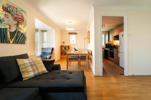 a living room with a black couch and a kitchen at Luxury Riverview 2Bed Apt- 5 mins from Excel London, Canary wharf, 02 Arena - Free Parking - PlayStation 4 Provided in London