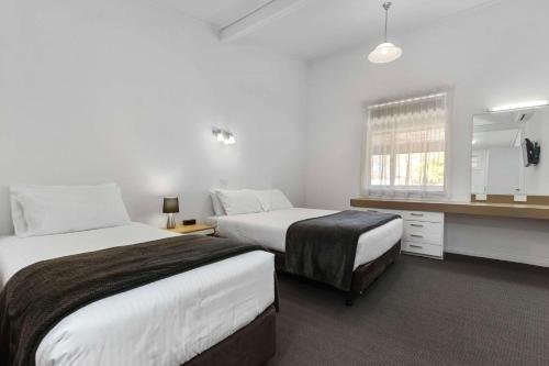 a hotel room with two beds and a desk and window at Econo Lodge East Adelaide in Adelaide