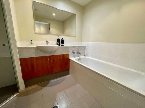W łazience znajduje się umywalka, wanna i lustro. w obiekcie North Sydney 2 Bedroom - Pool Parking Gym Spa Sleeps 6 w mieście Sydney